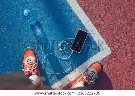 Sportsman POV on running sneakers, mobile phone with earphones and water bottle in golden hour time.
