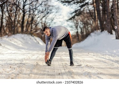 Sportsman In Shape Standing On Snowy Path In Nature And Doing Warmup And Stretching Exercises. Winter Fitness, Flexibility, Healthy Life