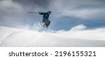 A sportsman skier in ski equipment jumps down a steep snowy slope of a mountain against the backdrop of a blue sky and snow-capped mountains. Winter risky sports, courage and speed concept