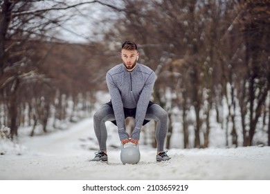 Sportsman Squatting On Snowy Path And Lifting Kettlebell. Outdoor Fitness, Winter Fitness, Bodybuilding