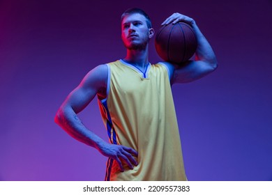 Sportsman. Studio shot of muscled man, basketball player standing with ball isolated on purple background in neon light. Concept of sport, achievements, competition, hobby, active lifestyle. - Powered by Shutterstock