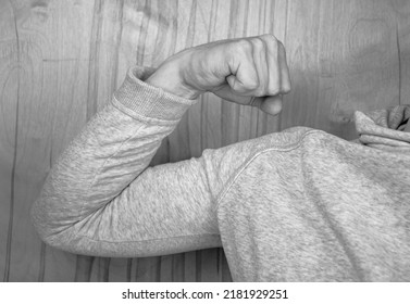 The Sportsman in a sweatshirt shows a muscle on his arm. Anonymous black and white photo. Athlete in a hoodie. Muscles of the hand. Sportsman in a sweatshirt.
