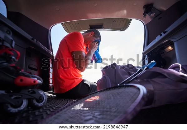 Sportsman wiping sweat with a towel sitting in\
trunk outdoors.