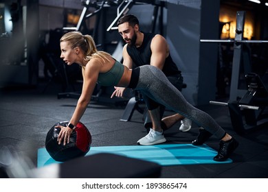 Sportsperson covering a medicine ball with her palms and raising her torso with a coach telling what to do - Powered by Shutterstock