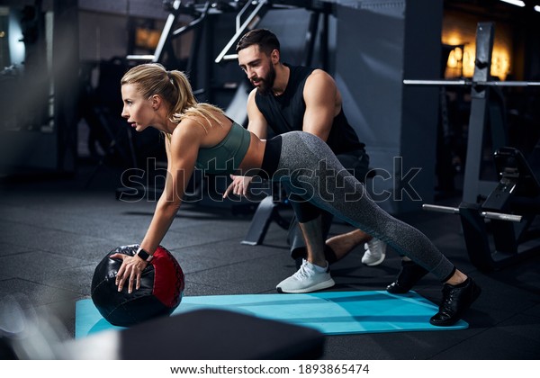 Sportsperson covering a\
medicine ball with her palms and raising her torso with a coach\
telling what to do