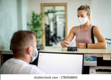 Sportswoman checking with smart phone at health club reception desk while wearing protective face mask.  - Powered by Shutterstock