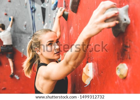 Sportswoman climber moving up on steep rock, climbing on artificial wall indoors. Extreme sports and bouldering concept