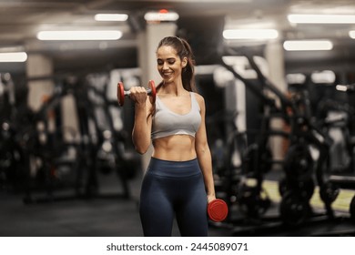 A sportswoman is doing dumbbells curls and flexing muscles in a gym. - Powered by Shutterstock