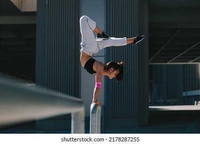 Sportswoman doing a handstand on railing outdoors. Flexible female athlete performing extreme sports in an urban space.