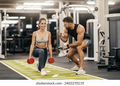 A sportswoman in shape is doing lunges with dumbbells while her trainer is counting in a gym. - Powered by Shutterstock