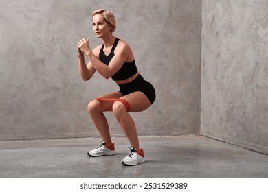 Sportswoman in shape is doing squats endurance with resistance band. Young sporty fit woman in sportswear squats with fitness elastic band on legs. - Powered by Shutterstock