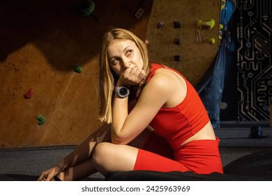 Sportswoman sits on mat thinking about upcoming climbing competition. Female athlete rests after bouldering session at indoor climbing gym - Powered by Shutterstock