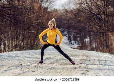 Sportswoman Standing On Snowy Path In Nature At Winter And Doing Stretching And Warmup Exercises. Flexibility, Winter Sport, Outdoor Fitness