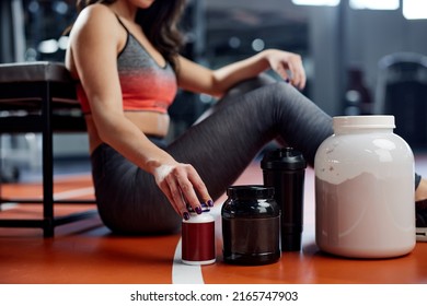 A Sportswoman Is Taking A Break In A Gym And Reaching For Supplements And Pre Workout Pills. Selective Focus On Hand With Bottle.