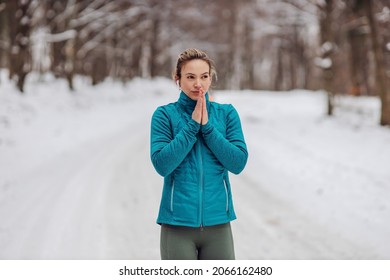 Sportswoman trying to warm up hands on snowy weather while standing in nature. Chilly weather, outdoor fitness, nature, winter fitness