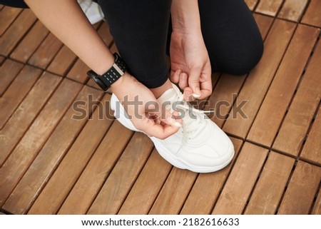 Sportswoman tying laces of her white snickers before morning run