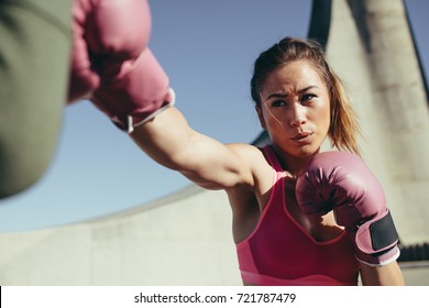 Sportswoman wearing boxing gloves training boxing. Strong female practicing boxing outdoors. - Powered by Shutterstock