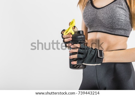 Sportswoman, wearing a grey top holding black bottle of water after tough workout, isolated