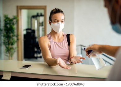 Sportswoman wearing protective face mask while receptionist in disinfecting her hands at the gym.  - Powered by Shutterstock