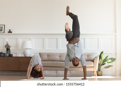 Sporty active african American father and preschooler daughter have fun practice gymnastics in living room, happy biracial dad and little girl child have fun play do exercised at home together