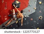 Sporty active businessman engaged in his hobby-bouldering. Equipped with belay system male athlete training in a colorful climbing gym, preparing to summer mountain ascend