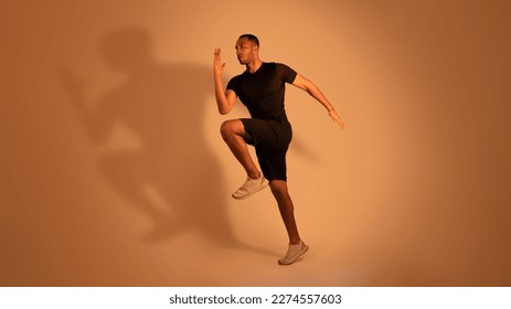 Sporty African American Man Standing Doing Elbow To Knee Crunches Or Jumping Exercising Looking Aside Over Beige Studio Background. Male Workout Concept. Panorama, Full Length Shot - Powered by Shutterstock