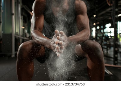 sporty african american man trains in dark gym and rubs his hands with magnesia, young guy makes clap with his hands in the fitness room, close-up of dust and flour with the hands of athlete - Powered by Shutterstock