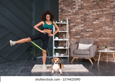 Sporty African-American woman with cute dog training at home