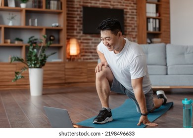 Sporty asian mature man exercising at home, stratching his legs, warming up before training and using laptop, watching fitness video on Internet or having online fitness class at home - Powered by Shutterstock