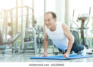 Sporty Asian Senior Man Push Up At The Gym. Happy Smiling Old Male Stretching Exercise And Workout. Sport, Recreation, Good Health. Copy Space.