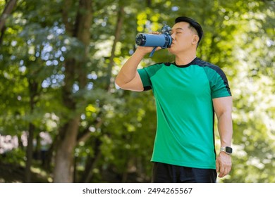 Sporty athletic thirsty guy Chinese man runner jogger drinking water after workout in park outdoors drink sport bottle, healthy habit active young Asian lifestyle refreshment hydration looking away. - Powered by Shutterstock