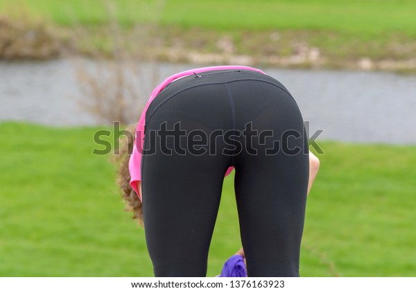 Sporty athletic woman bending\
over to remove her jacket while out jogging alongside a rural river\
in a close up rear view conceptual of a healthy active\
lifestyle