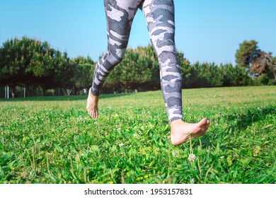 Sporty barefoot woman running on the green grass. Young female legs running barefoot