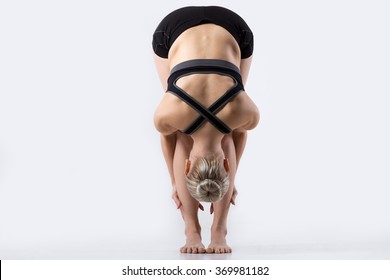 Sporty Beautiful Young Woman Practicing Yoga, Doing Uttanasana (intense Stretch Pose, Standing Forward Bend Or Head To Knees Pose), Working Out Wearing Black Sportswear, Studio, Full Length, Back View