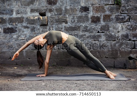 Sporty beautiful young woman practicing yoga working out, wearing sportswear, outdoor full length, brick wall