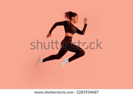 Sporty black lady jumping or running, posing in mid-air, exercising over peach neon background in studio, side view, full length, panorama with free space