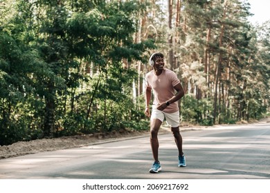 Sporty Black Man In Headphones Runs On The Road, Jogging Outdoors, Fitness Man Jogging In Nature, Young Fitness Man Running In The Morning Tropical Forest Trail