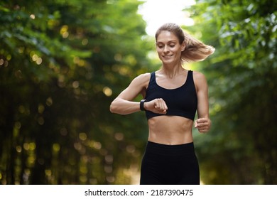 Sporty Blonde Lady Looking At Fitness Bracelet While Running Alone Outdoors, Smiling Middle Aged Woman In Sportswear Checking Tracker On Her Wrist, Exercising At Public Park, Copy Space