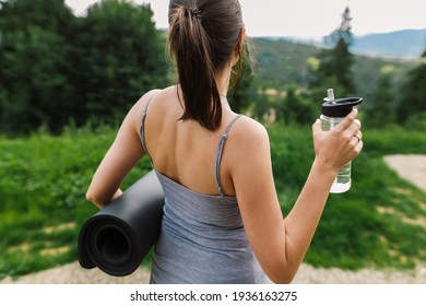 Sporty Casual Female Holding Yoga Mat And Bottle Of Water On Background Of Sunny Mountain Hills . Outdoor Workout. Healthy Lifestyle. Young Woman Relaxing After Training Among Trees