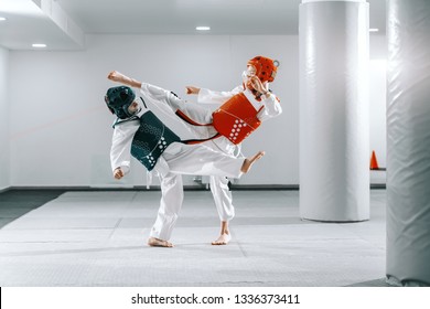 Sporty Caucasian Boys Having Taekwondo Training In White Gym And Kicking Each Other.