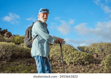 Sporty caucasian senior man with backpack smiling enjoying trekking day in countryside walking with hiking pole, Healthy lifestyle in retirement concept - Powered by Shutterstock