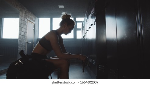 Sporty Caucasian woman sitting alone, leaving dark gym locker room feeling overwhelmed after bad day slow motion. - Powered by Shutterstock