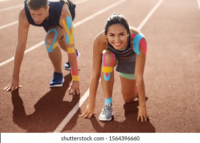 Sporty couple with physio tape in crouch start position at stadium