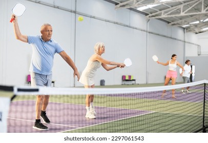 Sporty couple of senior woman and man playing doubles pickleball on indoor court, ready to hit ball. Sport and active lifestyle concept.. - Powered by Shutterstock