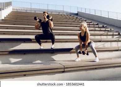 Sporty couple in sportswear doing squats with dumbbells outdoors on city stairs