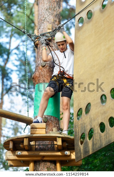 sporty, cute, young boy in white t shirt in the\
adventure rope activity park with helmet and safety equipment. Boy\
plays and has fun doing activities outdoors. Hobby, active\
lifestyle concept