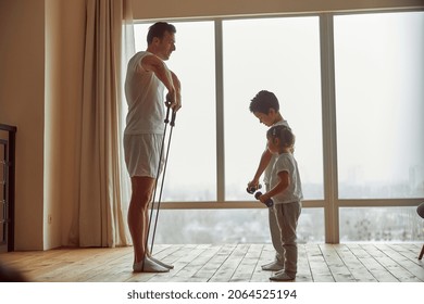 Sporty Dad Is Using Resistance Bands While Doing Training With Daughter And Son Before Window