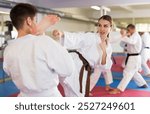 Sporty determined young woman in kimono practicing kicking technique paired with male partner in martial arts training room