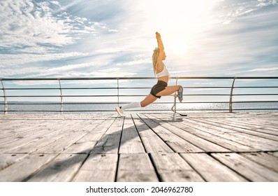 Sporty disabled athlete woman in sportswear with prosthetic leg standing in yoga pose on the bridge in front of the sea. Copy space. Full length. Side view. - Powered by Shutterstock