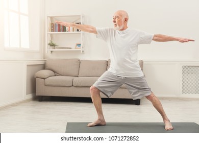 Sporty Elderly Guy Practicing Yoga Indoors. Senior Man Doing Stretching Exercise At Home. Active Lifestyle And Healthcare In Any Age, Copy Space